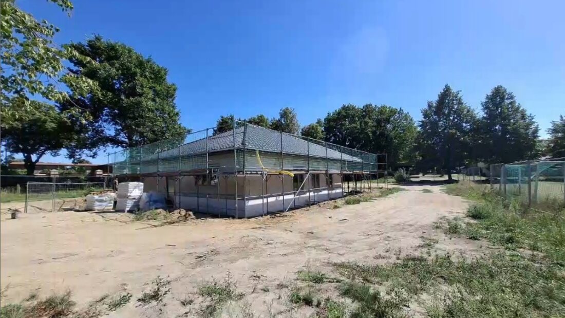 Ein langgestrecktes Gebäude im Rohbau mit Gerüst und Baumaterialien auf einer Baustelle.