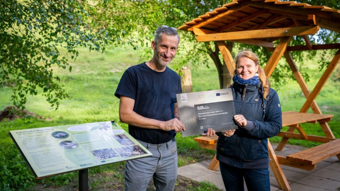 Guido Herbst, Gemeindevertreter und Frau Nicole Schwarz, die Bürgermeisterin der Gemeinde Liepe, halten gemeinsam die Fördermittelhinweise in der Hand.