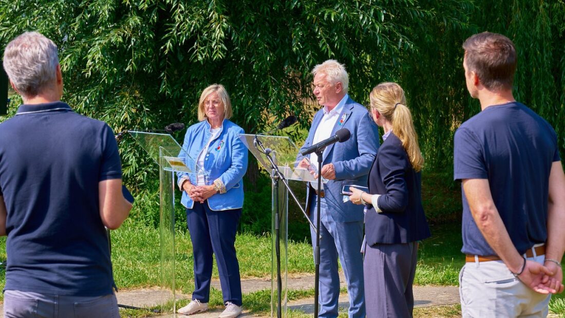 Zwei Personen stehen an Rednerpulten und sprechen zur Presse.
