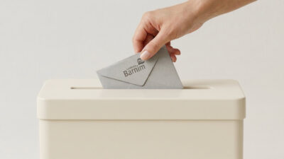 Hand die einen Wahlbrief in eine Wahlurne steckt.