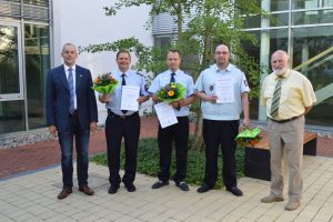 Fünf Personen mit Urkunden und Blumensträußen