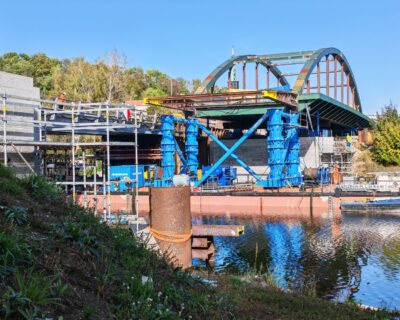 Reparatur einer Stahlbrücke über einen Fluss mit blauen Stützpfeilern und Gerüsten.
