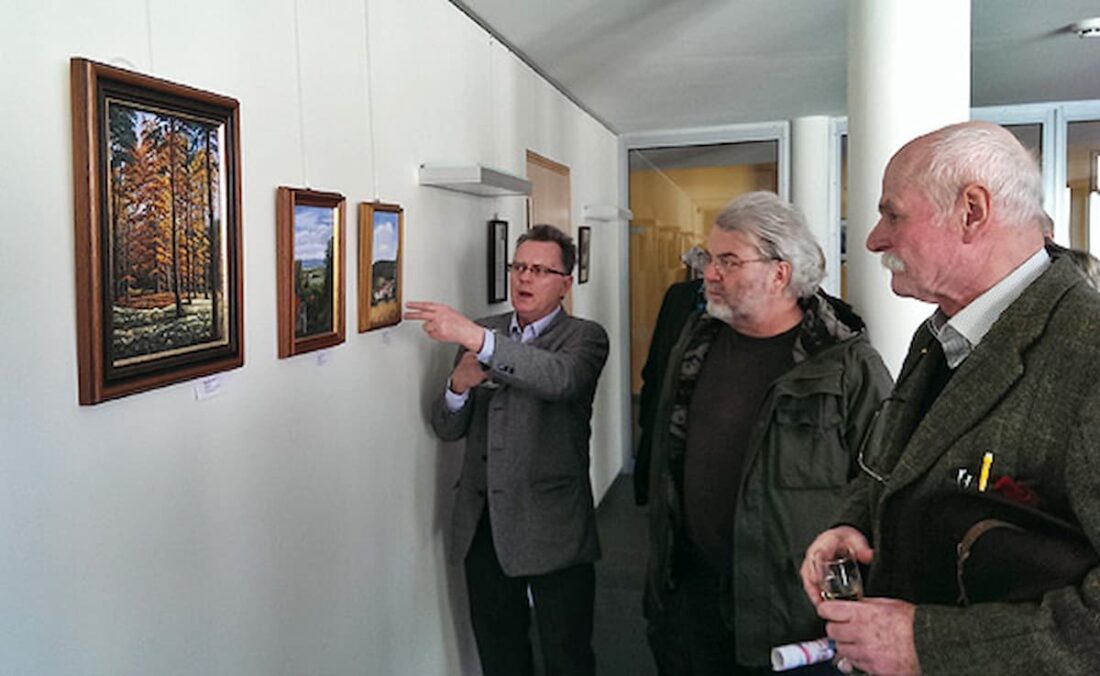 Drei Personen vor Bildern an einer Wand.