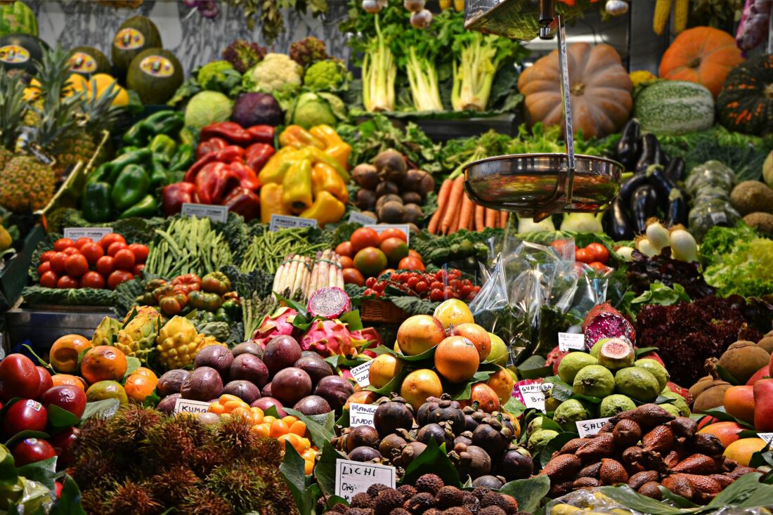 Gemüsestände und Obststände mit Kürbissen, Kohl, Trauben, Äpfeln, Tomaten, Ingwer und weiteren Sorten auf einem Markt.