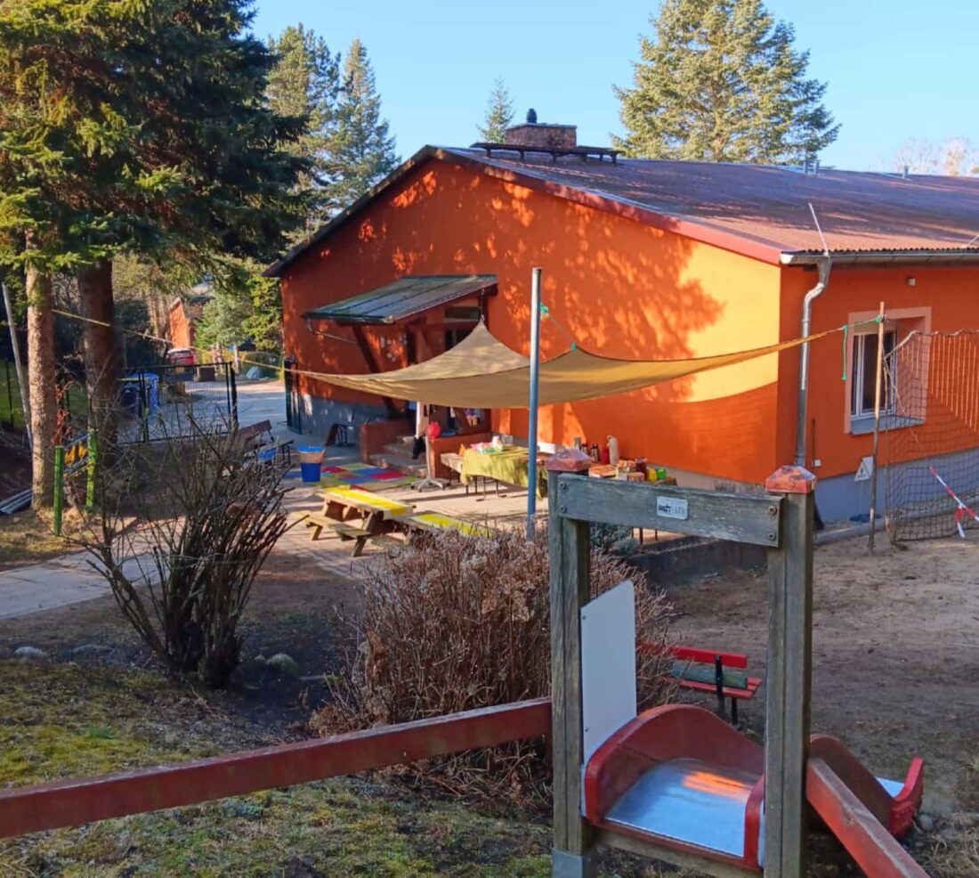 Orangefarbener Flachbau mit einem Spielplatz im Vordergrund.
