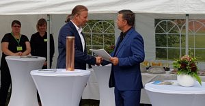 Zwei Personen. Eine übergibt der anderen einen Bescheid.